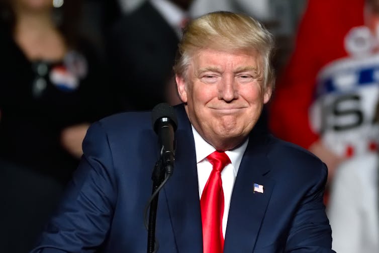 Blonde elderly man (Donald Trump) in a red tie and blue suit and big hair.