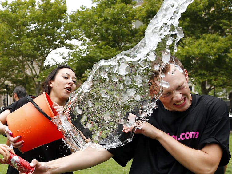 Person sluicing a bucket of ice water over another person's head
