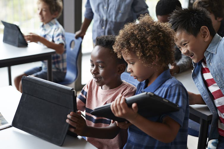 Two boys look at the screen of a digital tablet in a classroom.