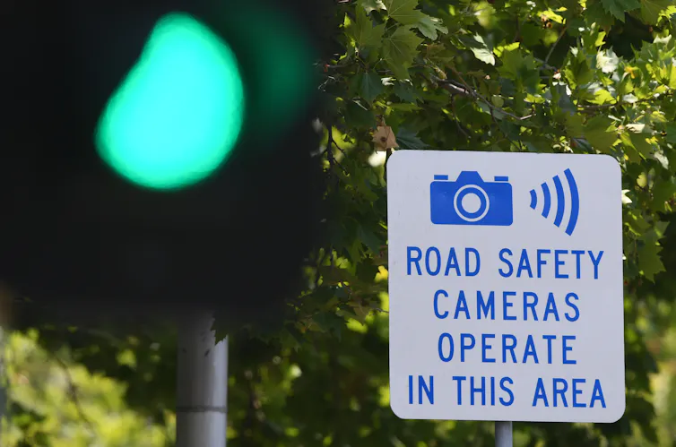 A green traffic light in front of a sign that says 'road safety cameras operate in this area'