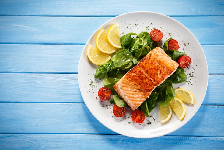Plate of salmon on bed of green salad, with lemon slices, on blue wood table