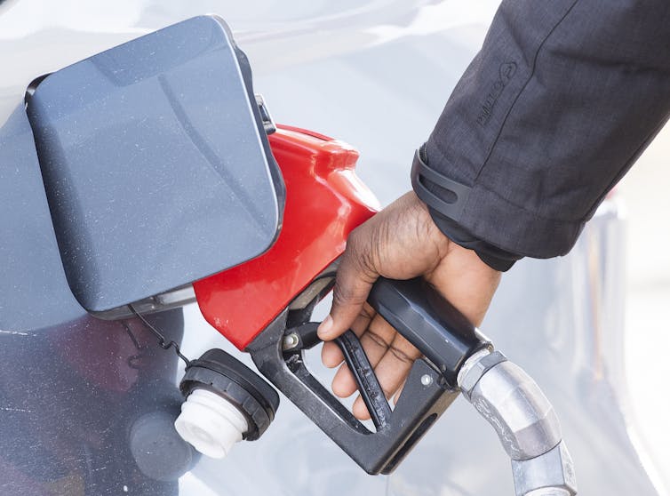 A hand holding a gas nozzle that is pumping gas into a car