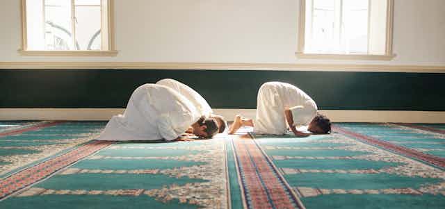 Three men in white robes kneeling for prayer in a mosque