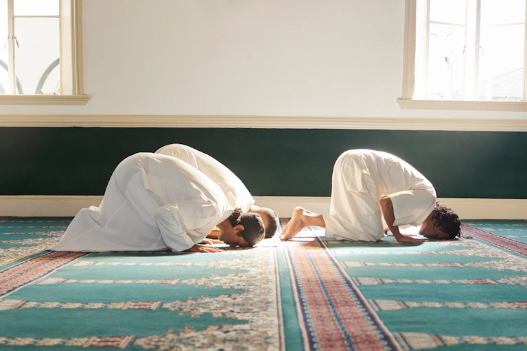 Three men in white robes kneeling for prayer in a mosque