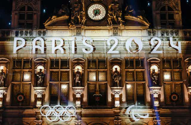 A French building lit up with 'Paris 2024' signage and the Olympic rings