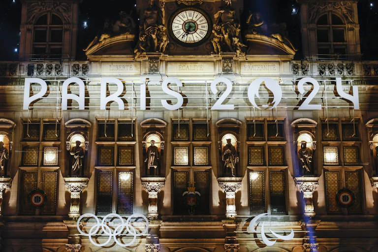A French building lit up with 'Paris 2024' signage and the Olympic rings