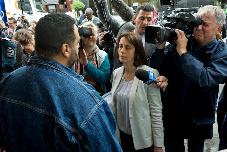 Person facing journalists with cameras and microphones.