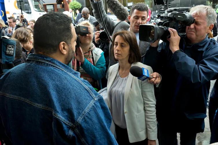 Person facing journalists with cameras and microphones.