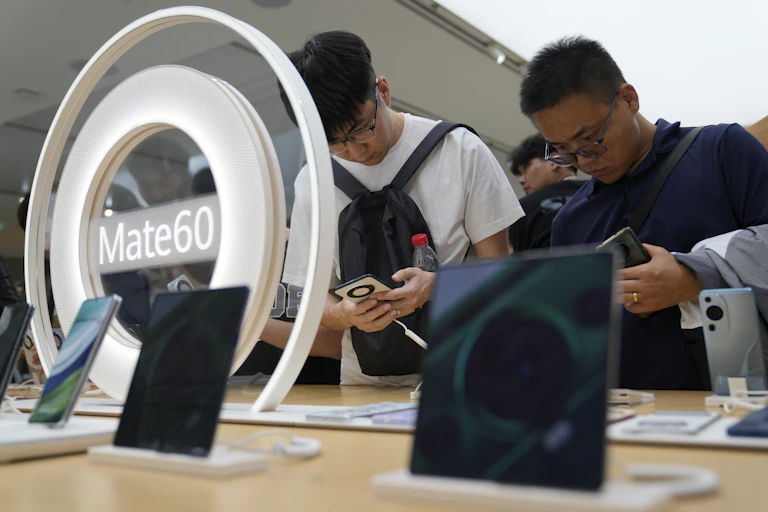 Two men pore over mobile phones with the Mate60 logo in front of them on a table.