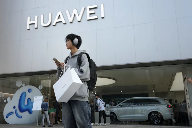 A man wearing headphones carrying shopping bags stands outside a Huawei store.