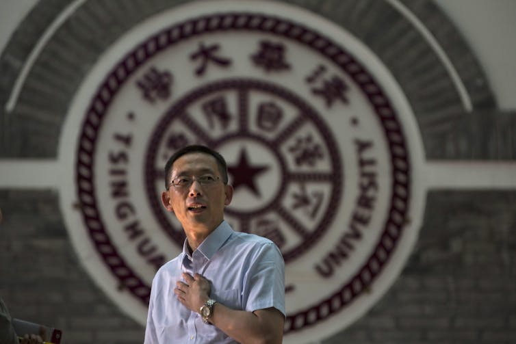 A man stands in front of a university logo.