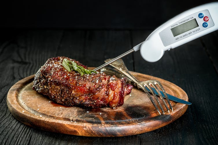 Un asado sobre una tabla para cortar con un termómetro para carnes