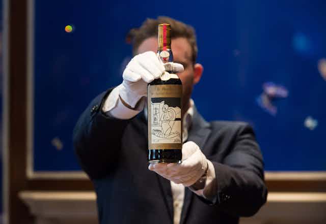 Man wearing white gloves presents a bottle of whiskey.