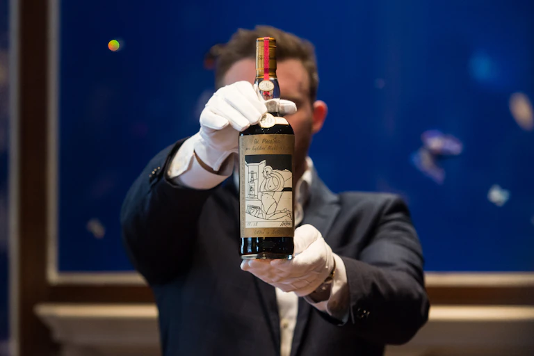 Man wearing white gloves presents a bottle of whiskey.