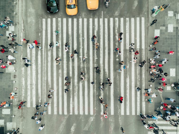 Aerial view of pedestrians on a crosswalk, a few cars waiting at the edges