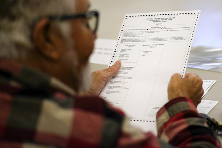 A person in a checked jacket holding a ballot.