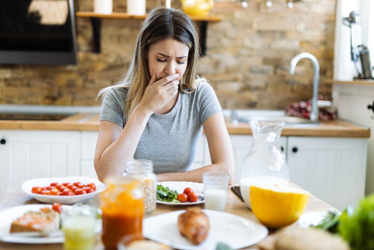 Woman covering her mouth at the breakfast table as though she's about to be sick.