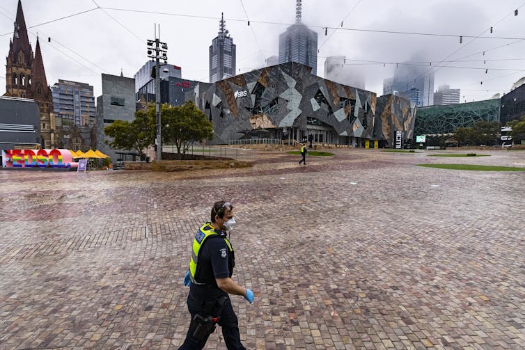 A masked police officer walks across a deserted city square during a COVID lockdown.