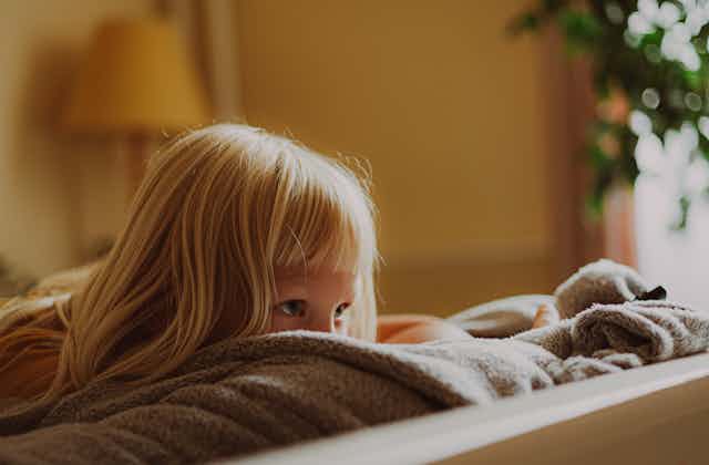 A young girl peeks over the top of a couch. 