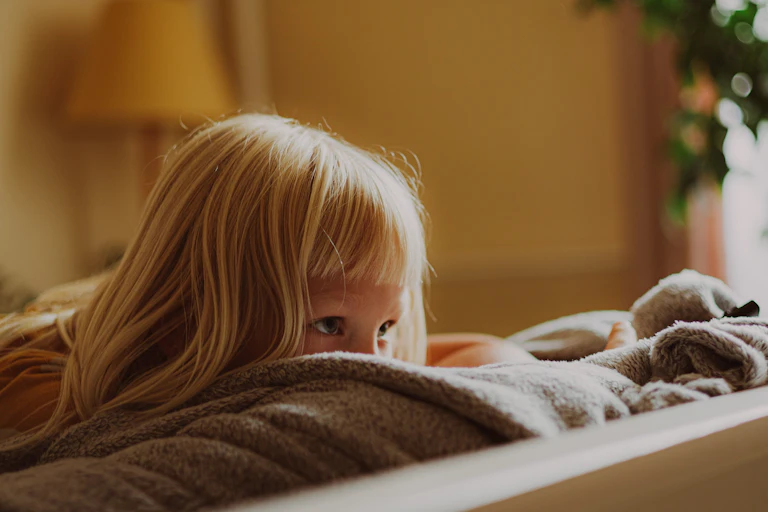 A young girl peeks over the top of a couch.