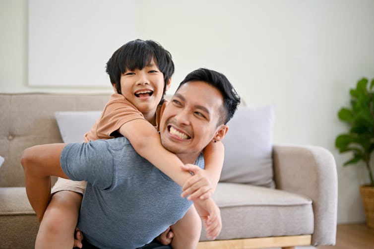 An Asian man playing with a young boy. Both are smiling