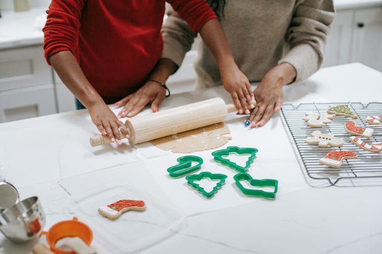 A mother and child roll dough to make Christmas cookies.