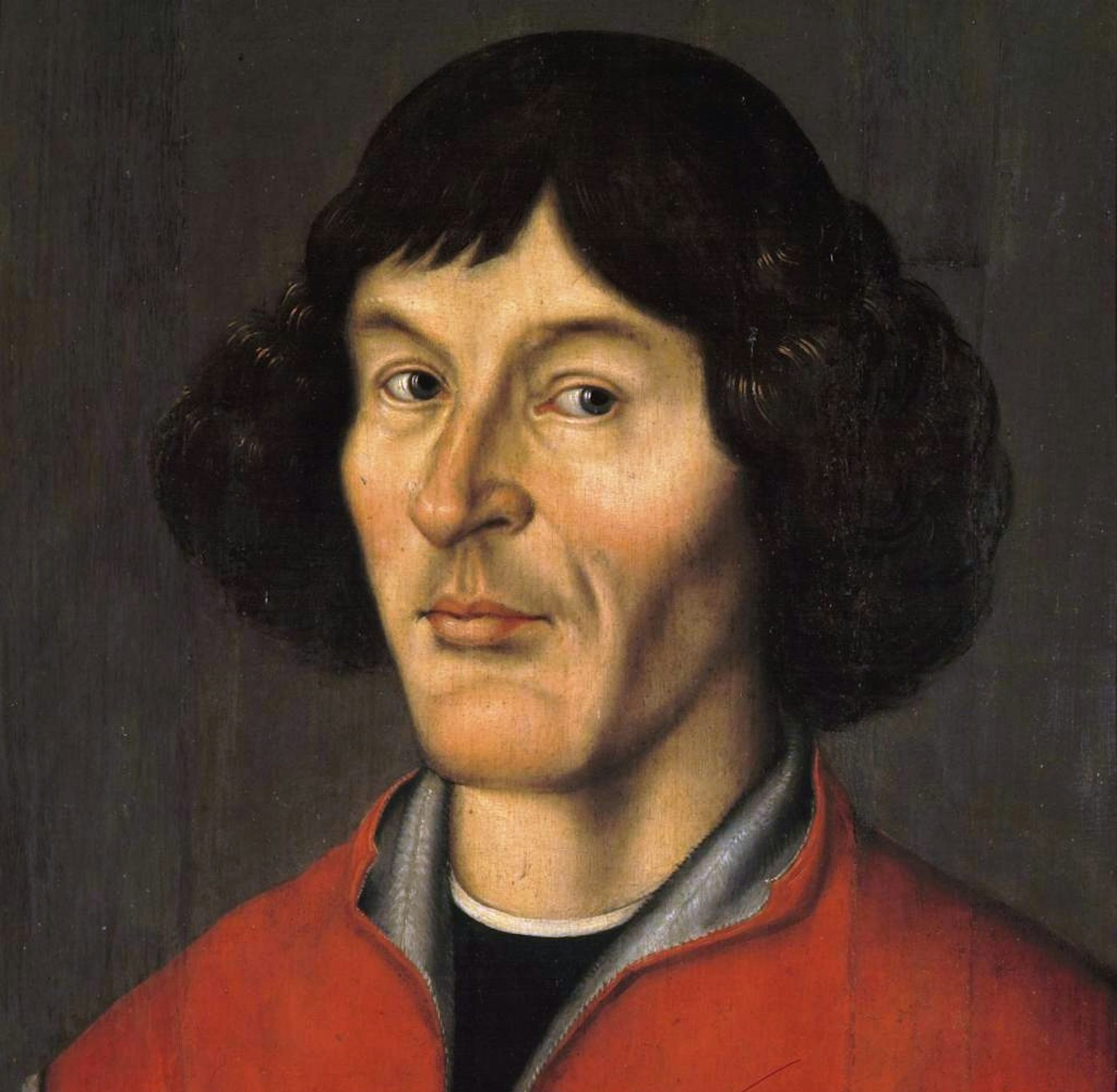 Closeup of a man in a red jacket, with longish hair and looking determined.