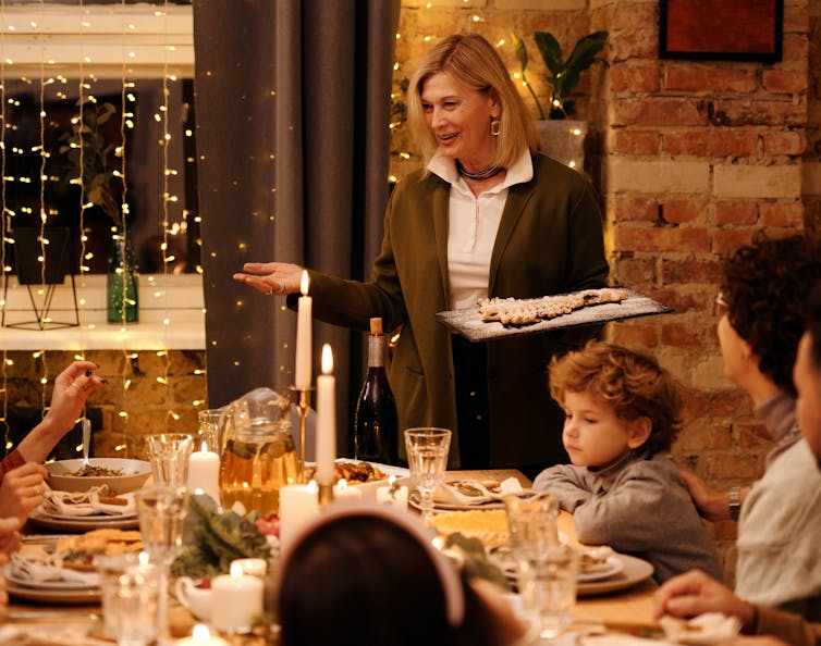 A family, including a small child, seated around a Christmas table, decorated with candles and fairy lights.