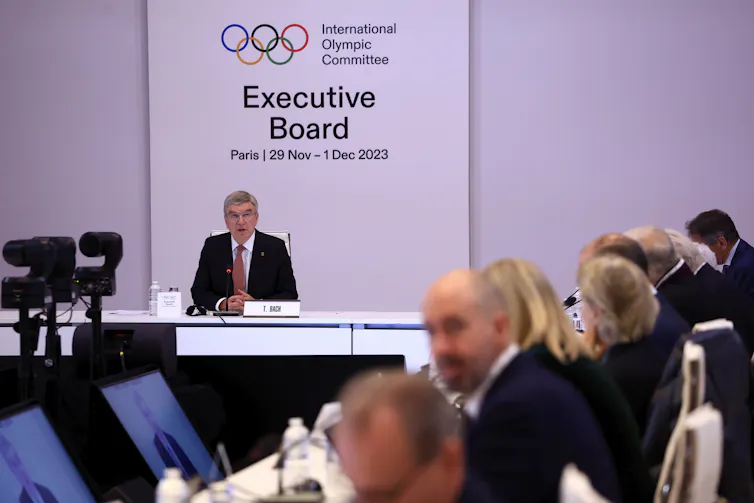 A man sitting in front of a large sign reading 'Executive Board' and the Olympic rings.