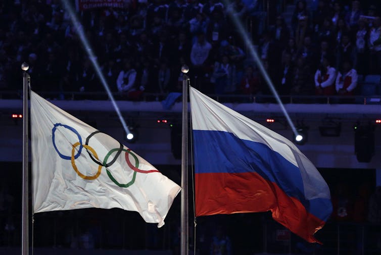An Olympic flag flies next to a Russian flag.