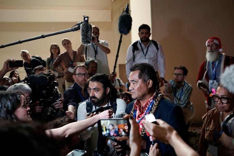 A man surrounded by cameras and microphones.