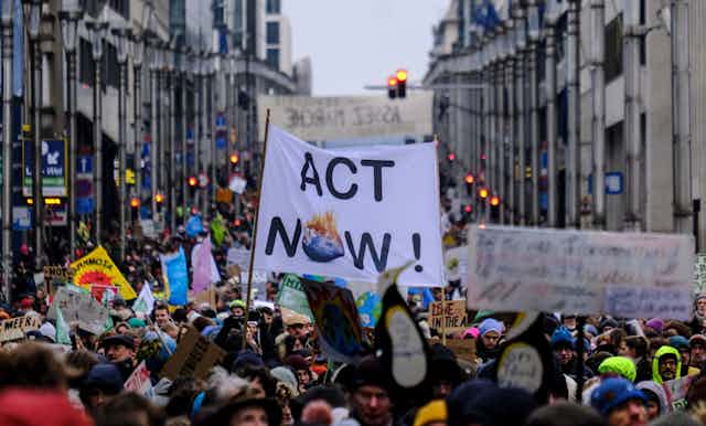 Participantes en una manifestación sostienen una pancarta que dice "act now".