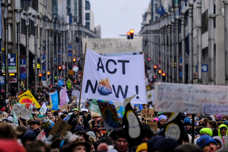 Participantes en una manifestación sostienen una pancarta que dice "act now".