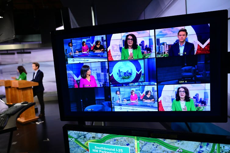 Two people standing at lecterns and a studio monitor showing nine different pictures on it.