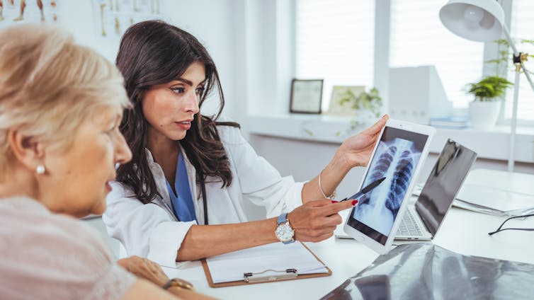 A female doctor explains lung x-ray results to older female patient.