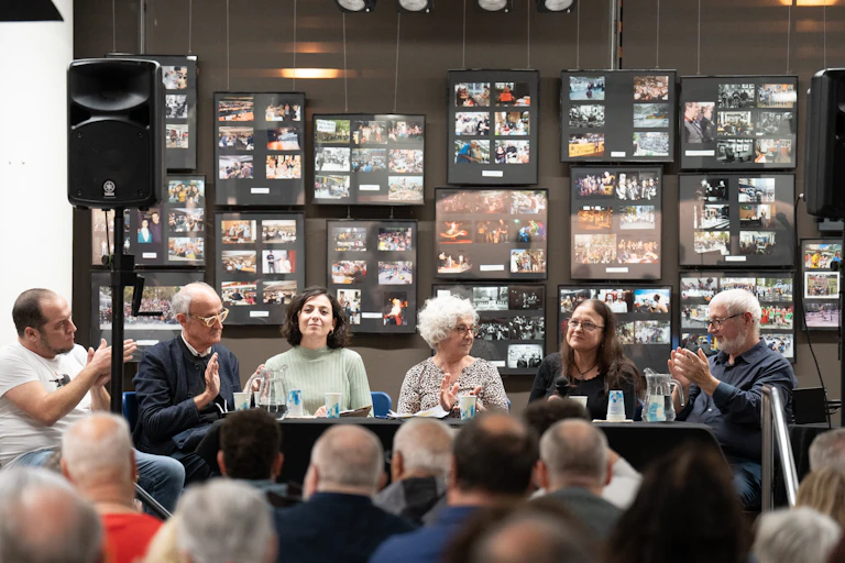 A group of people sit at a table in front of a wall of images.
