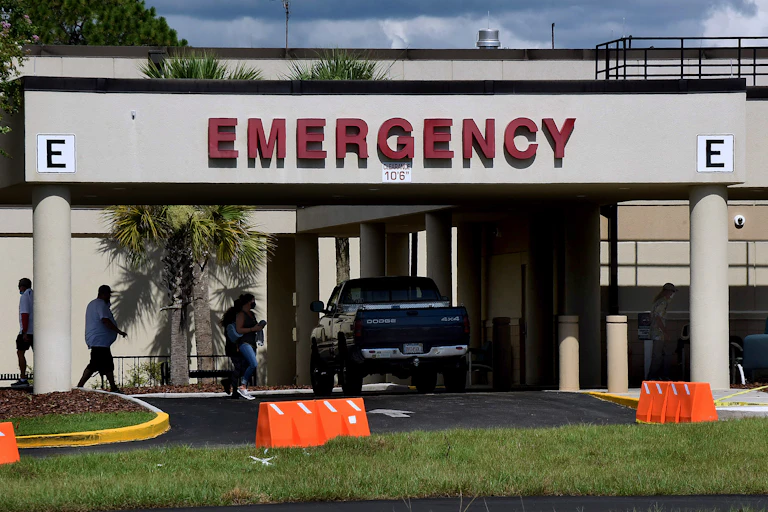 People walking past parked pickup truck into a hospital emergency room entrance