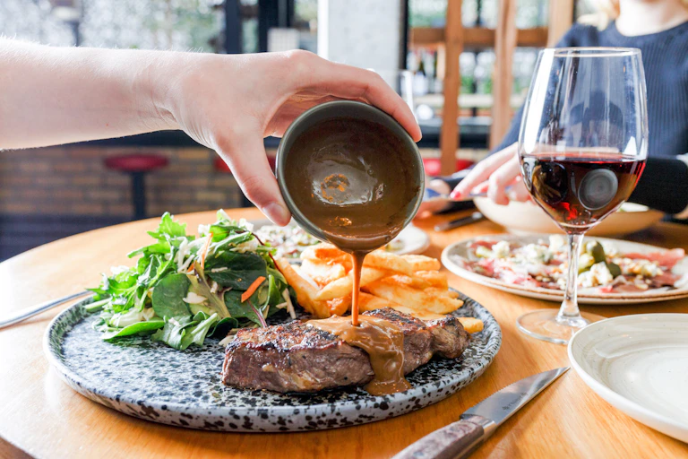 A person pours gravy onto a piece of roasted meat.