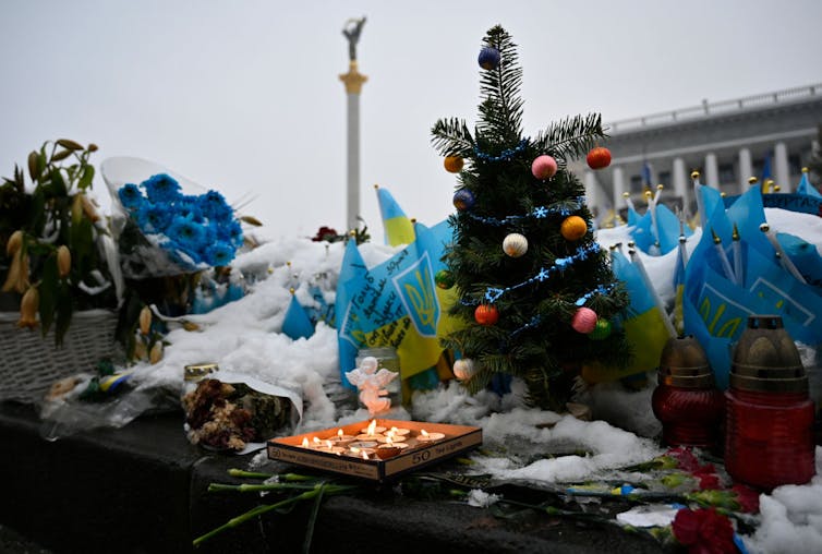 Blue and yellow decorations, along with a tiny Christmas tree and candles, positioned on snow with a large monument in the background.