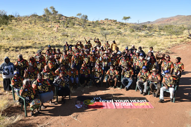 A group of First Nations people together, around a banner that reads 'open your heart to our voice.'