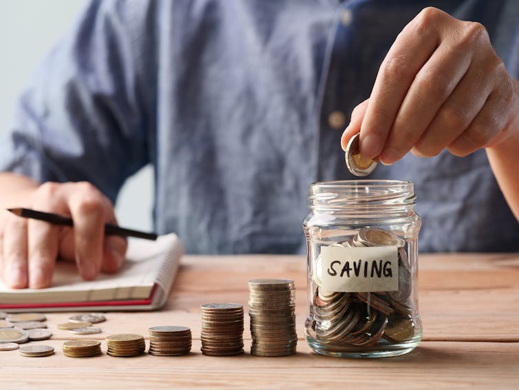 Unidentified man taking notes as he puts money into a jar