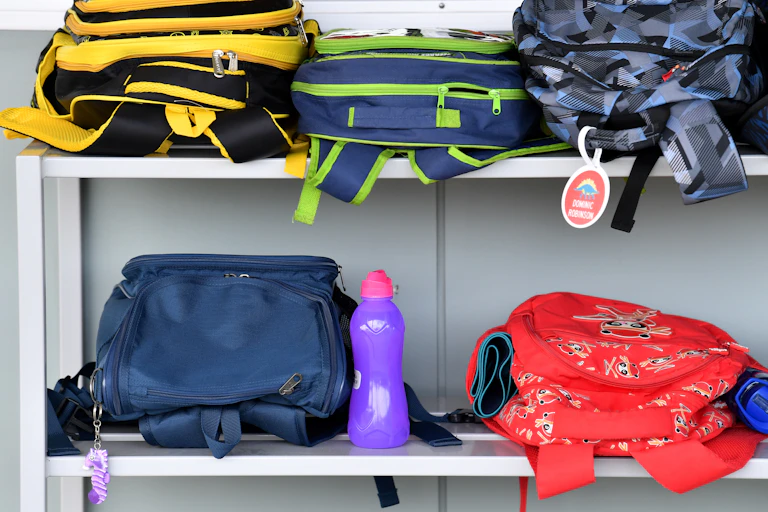School backs stacked on a shelf outside a classroom.