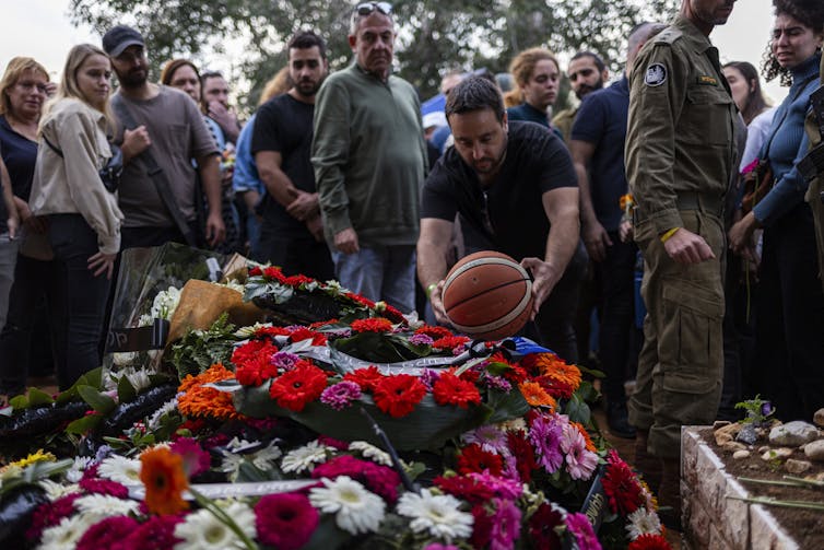 A man lays a basketball on a coffin, covered in flowers