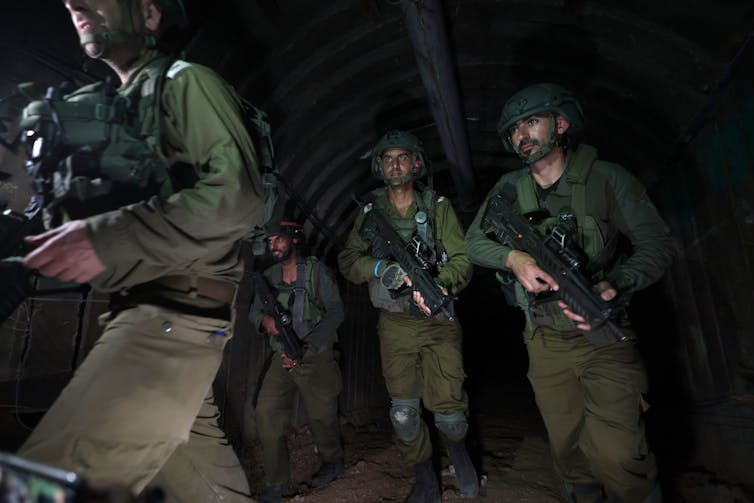 Four armed soldiers walk through a dark tunnel