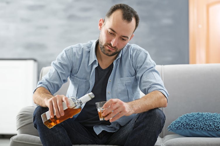 Man sitting on a sofa pouring hard liquor from a bottle.