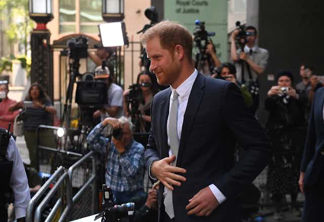 Prince Harry leaving the Royal Courts of Justice while press photographers take shots of him.