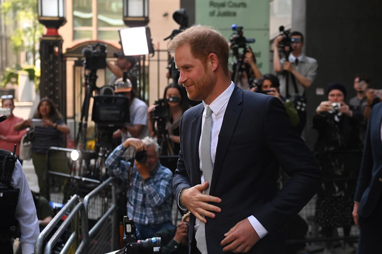 Prince Harry leaving the Royal Courts of Justice while press photographers take shots of him.