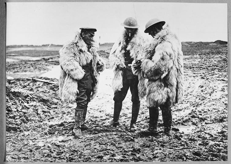Black and white photo of three soldiers in heavy sheepskin coats and helmets, smoking cigarettes
