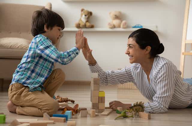 A woman and child high-fiving while playing with blocks on the floor