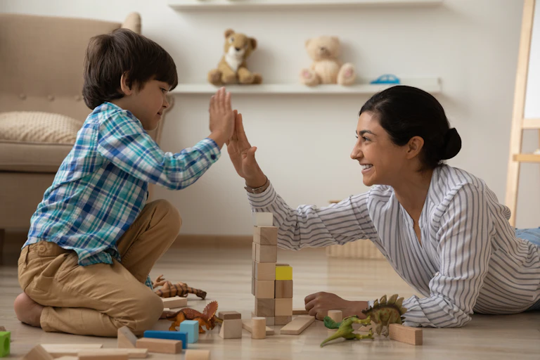 A woman and child high-fiving while playing with blocks on the floor